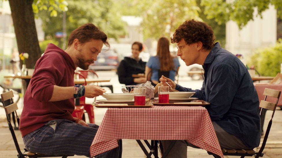 Kieran Culkin and Jesse Eisenberg eating lunch outdoors in A Real Pain