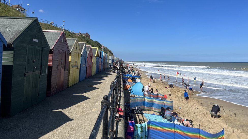 Mundesley seafront with beach huts and bathers on beach