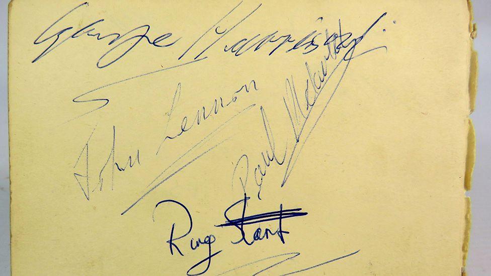 The signatures of the four members of The Beatles in blue ink on yellow paper.