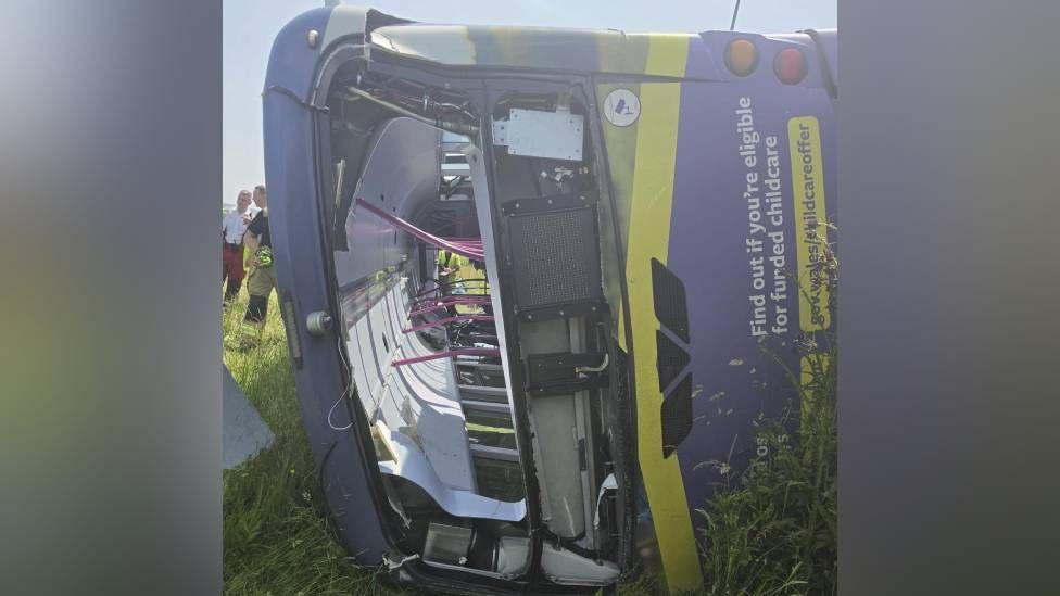 A purple bus is seen lying on its side in a field