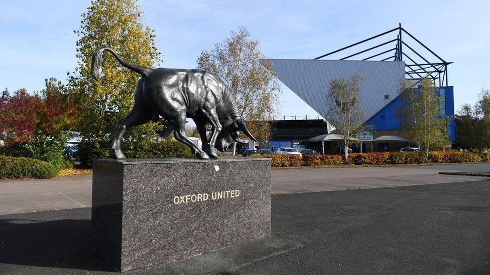 The Kassam Stadium with a statue of a bull in front of the building. Photographed on a sunny day.