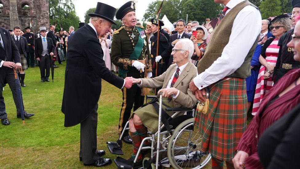 King Charles shaking hands with a man in a wheelchair at the royal garden party in Holyrood Park, Edinburgh.
