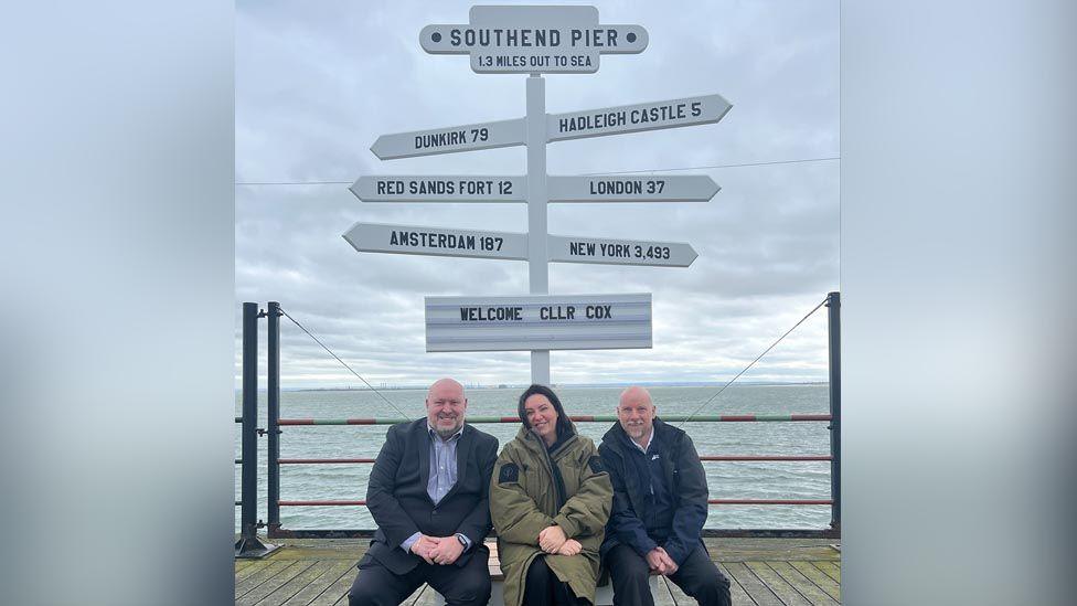 Two men and one women sitting in front of new selfie signpost at Southend-on-Sea pier