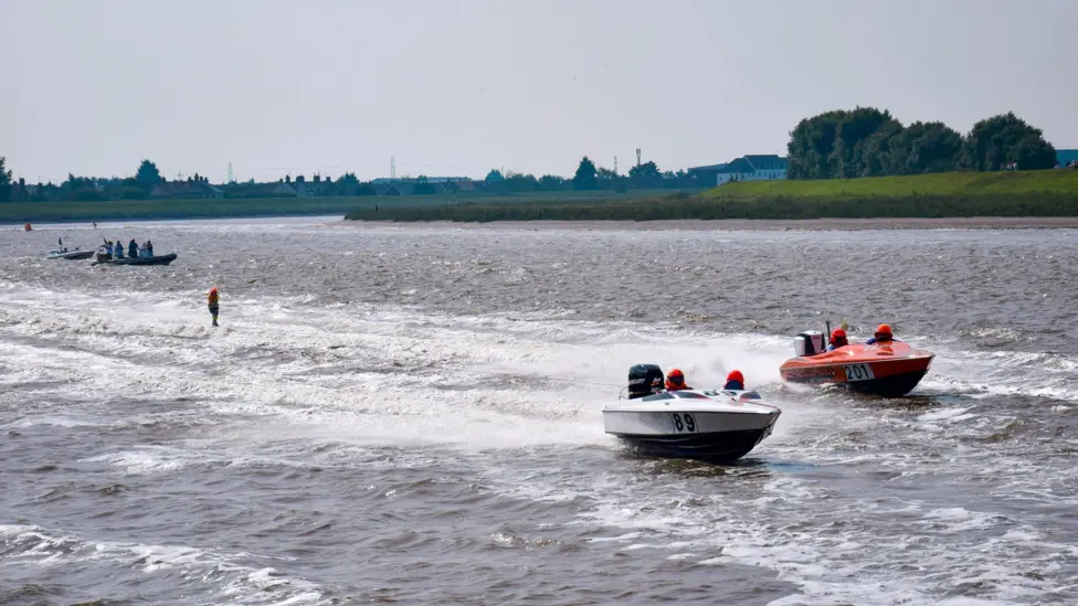View of two small boats - one white, one red, racing along the River Great Ouse.