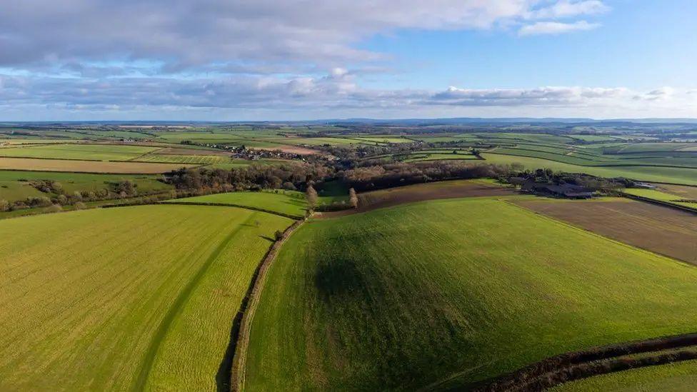 A drone shot of sweeping Dorset countryside. The sky is cloudy and the ground a mix of green and brown fields.