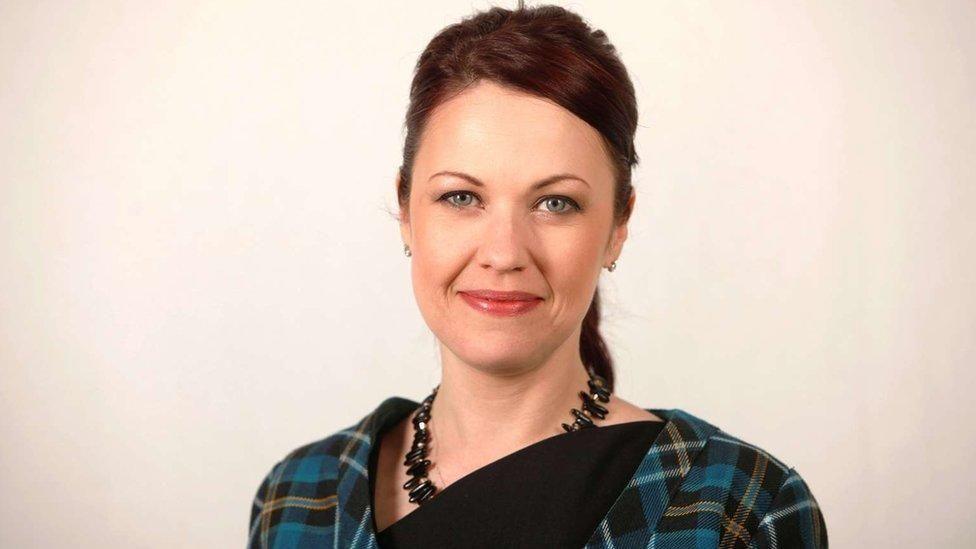 Studio head-and-shoulders shot of former SNP MSP Gail Ross. Her brown hair is combed tight in a ponytail. She is smiling and wearing a green tartan dress with a gemstone-style necklace.
