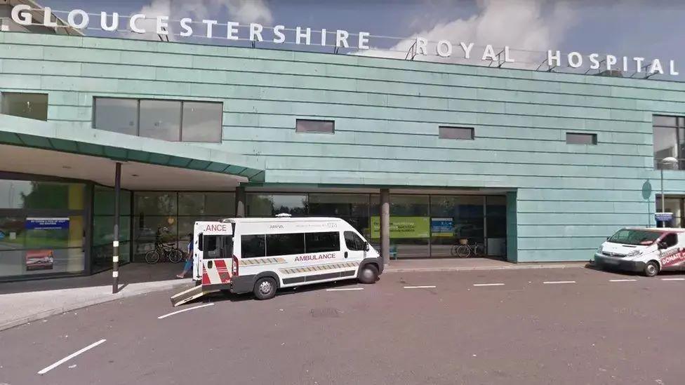 External shot of a white ambulance outside Gloucestershire Royal Hospital, which has a green, cladded facade