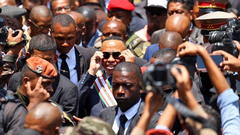 Col Michael Randrianirina in a media scrum smiles as he adjusts his sun glasses outside the High Constitutional Court.