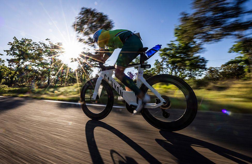 Wilhelm Hirsch of Germany competes in the bike leg during the 25 Ironman 70.3 Aix-en-Provence in France with bright sunshine being illuminated through trees and onto the road. Photo by Jan Hetfleisch