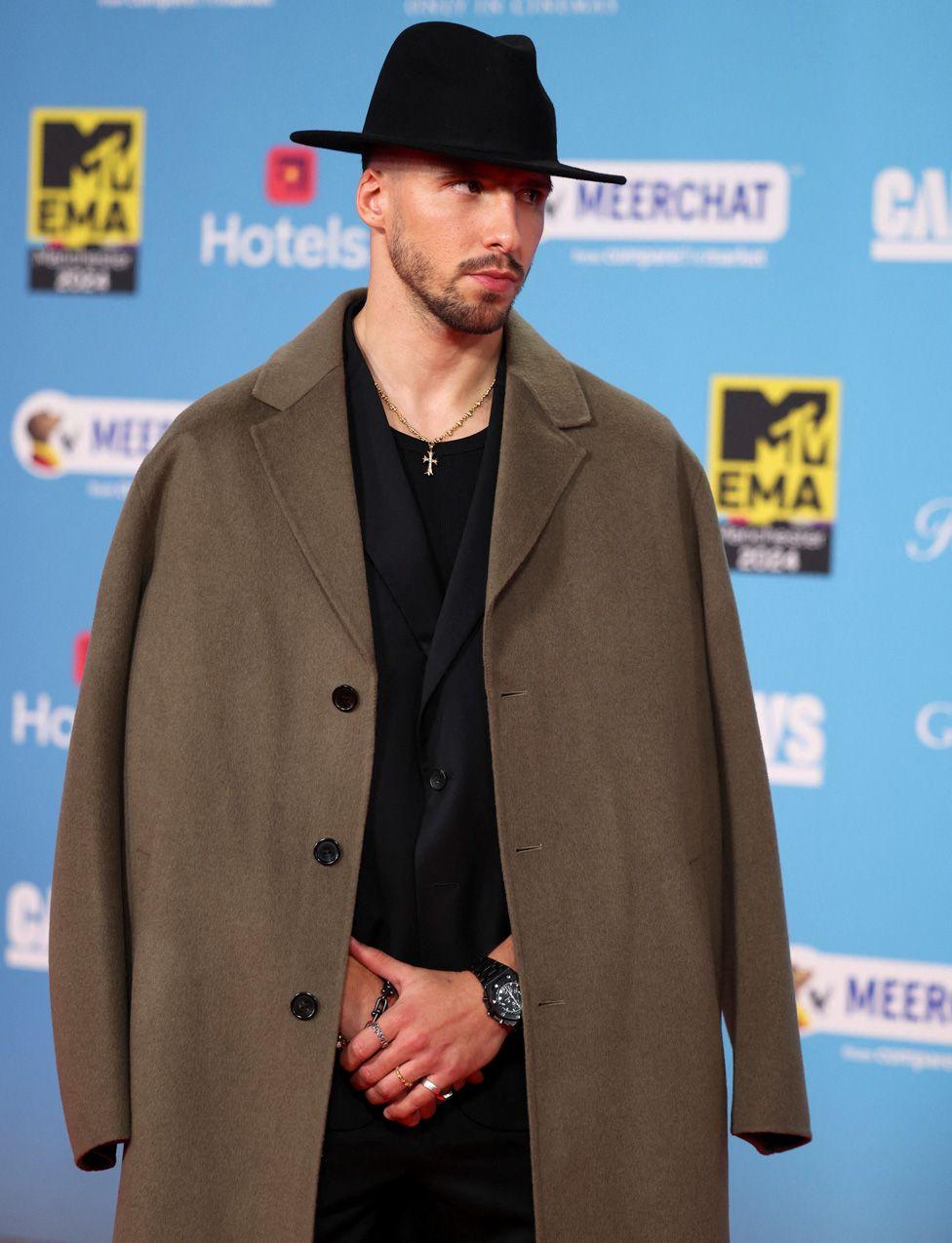 Ruben Dias in a long brown overcoat and black shirt and hat