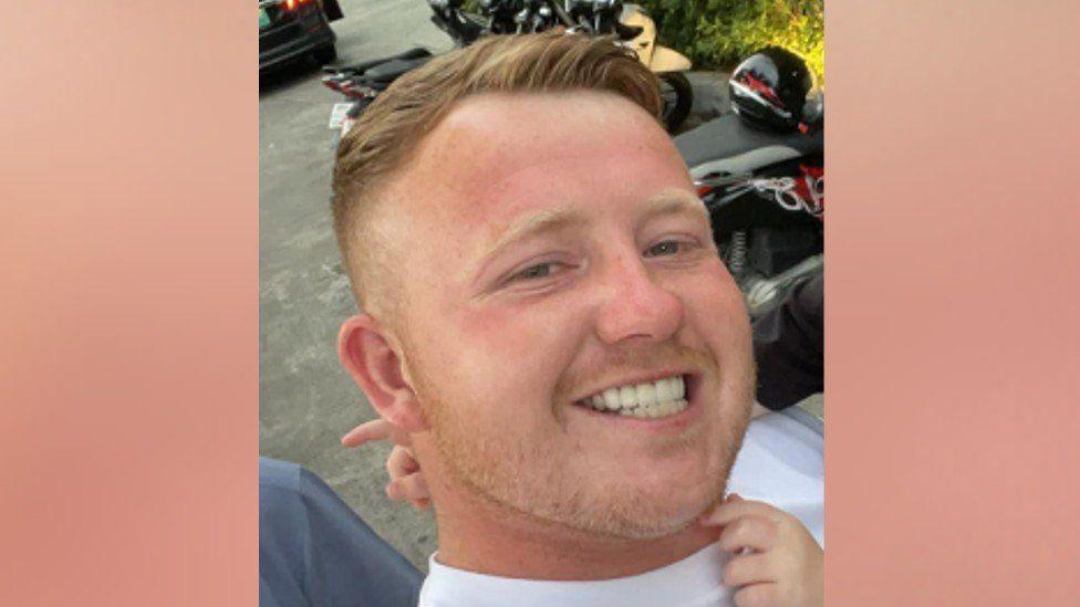 A headshot selfie of Tommy Hunter, stood in front of motorcycles