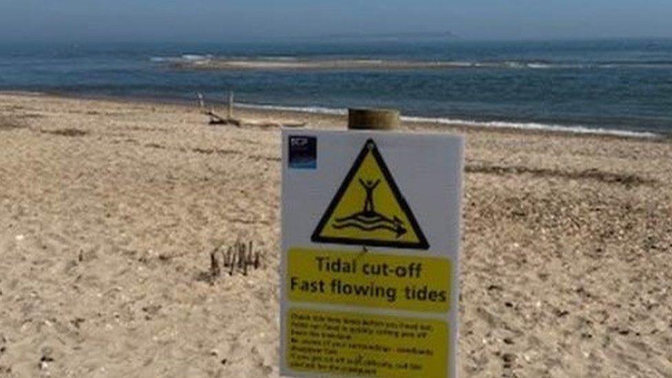 A sandy beach with a warning sign on wooden post and sea behind.