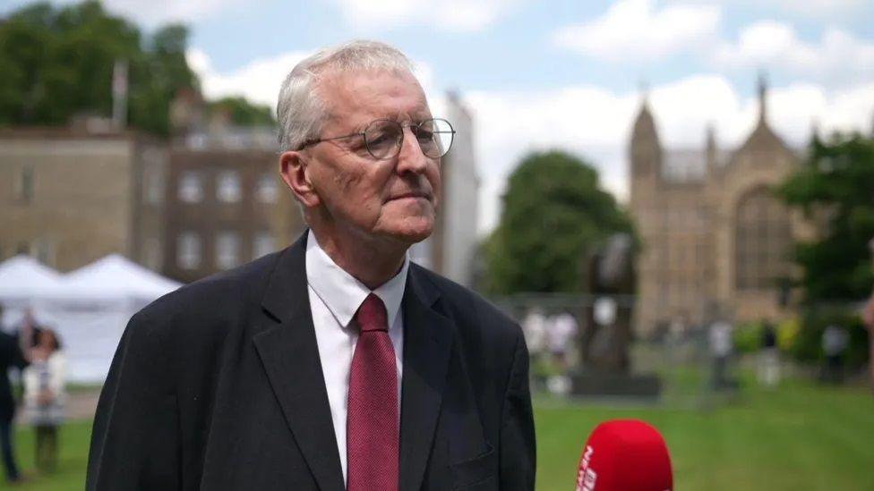 Hilary Benn speaking to reporters outside Westminster in black suit white shirt and red tie