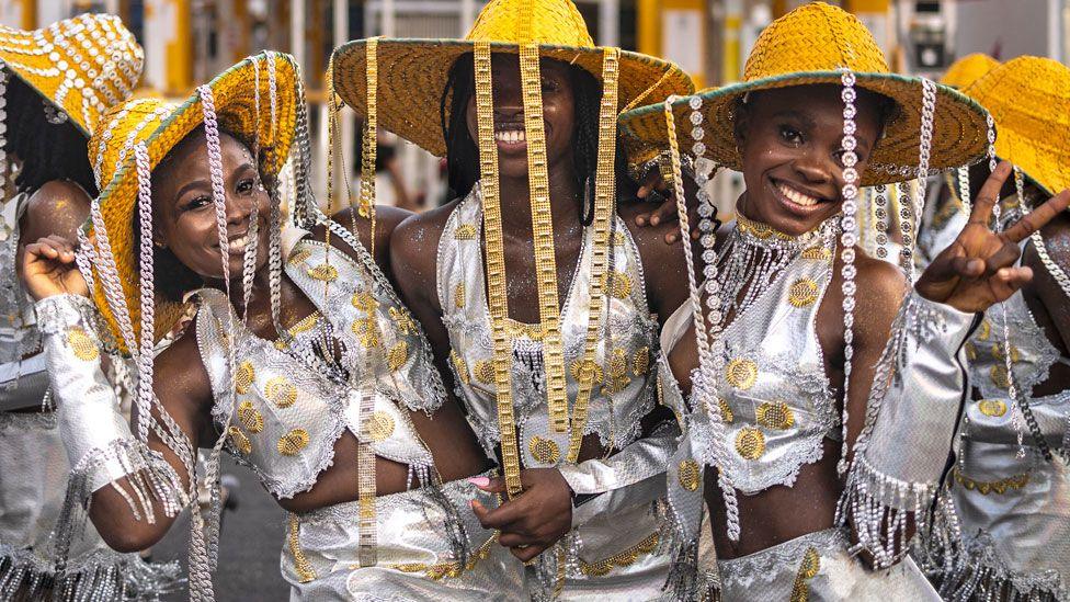 Women in silver outfits and gold-brimmed straw hats with chains hanging from their smile as they pose for the camera in Calabar, Nigeria