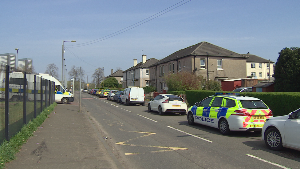 A street with several police cars and vans all parked in front of houses