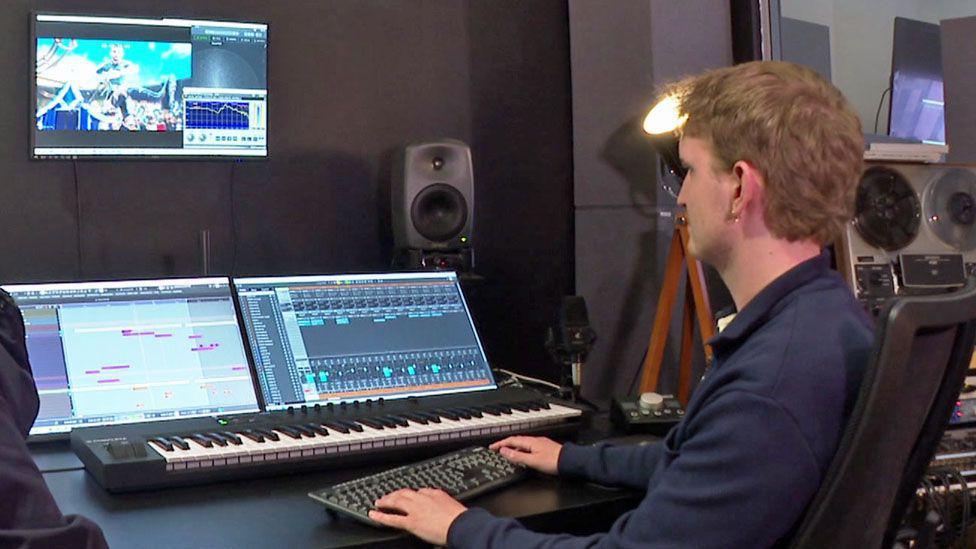 Greg Owens sitting in a studio in front of a sound desk, a keyboard and three monitors, showing the BBC's Euros 2024 pinball-themed trailer