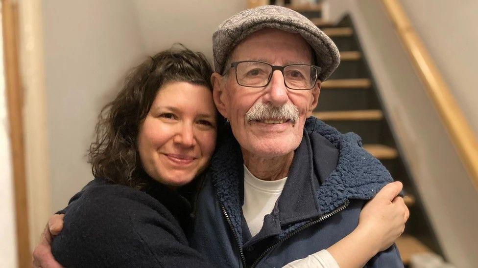 Sharone and Oded hugging each other and smiling. Photo taken in a house. 