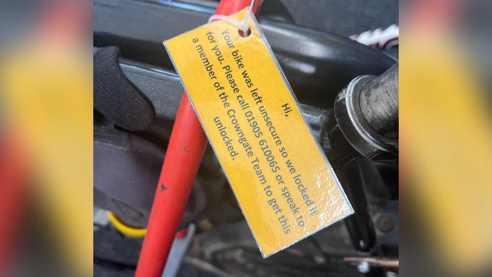 A close up of a laminated card which reads: "Hi, Your bike was left unsecure so we locked it for you. Please call 01905 610065 or speak to a member of the Crowngate Team to get this unlocked."