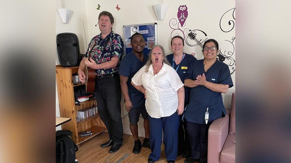 Marcus Brown performing with a guitar at Clifton Lodge, with staff joining in to sing for residents and their families