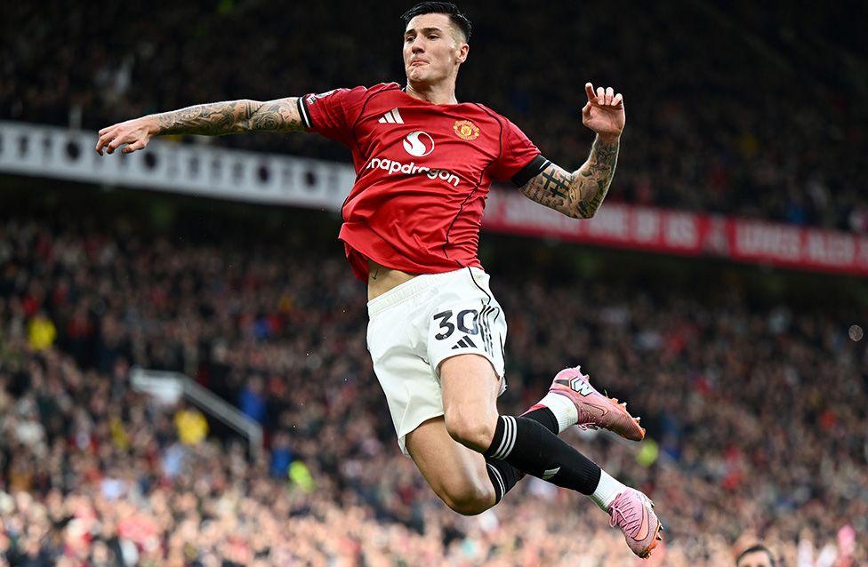 Manchester United's Benjamin Sesko celebrates scoring his team's second goal during the Premier League match against Sunderland at Old Trafford. Sesko leaps mid-air in a red Manchester United jersey and white shorts, arms extended, legs bent, pink boots visible, with a packed stadium crowd in the background.