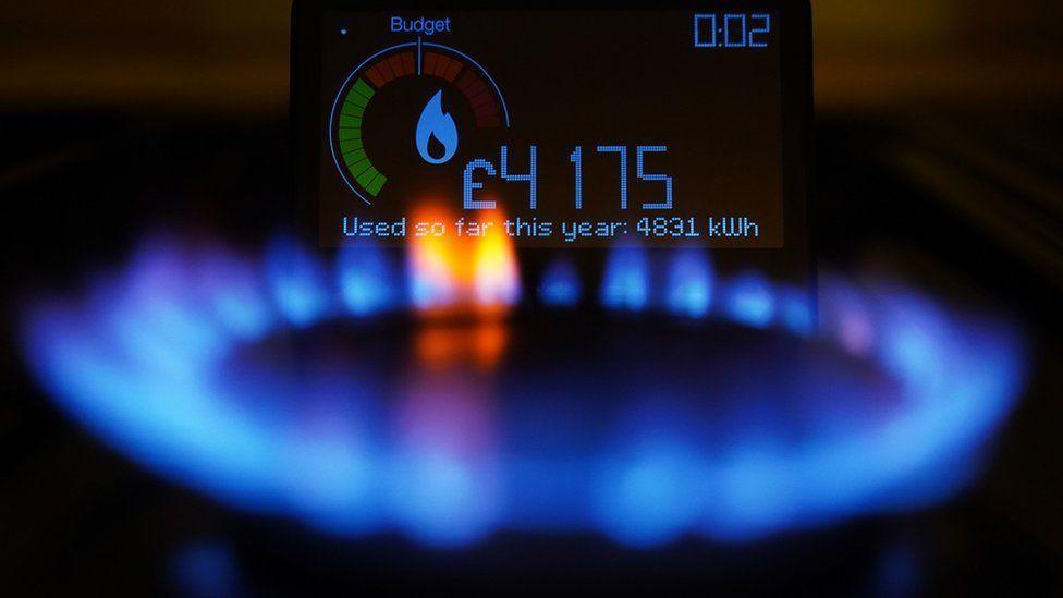 A burning hob gas ring with a smart meter display behind it