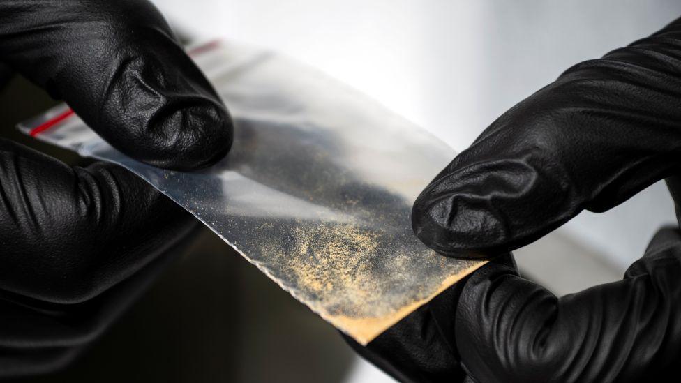 Hands wearing back gloves hold nitazene powder