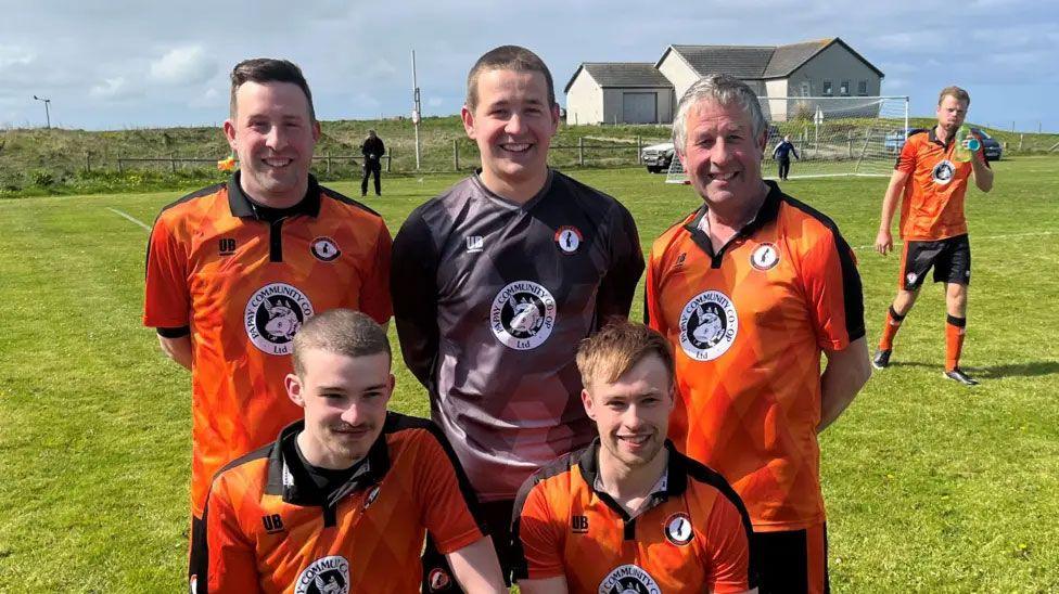 A group of five footballers in orange strips and one in a goalkeeper's top