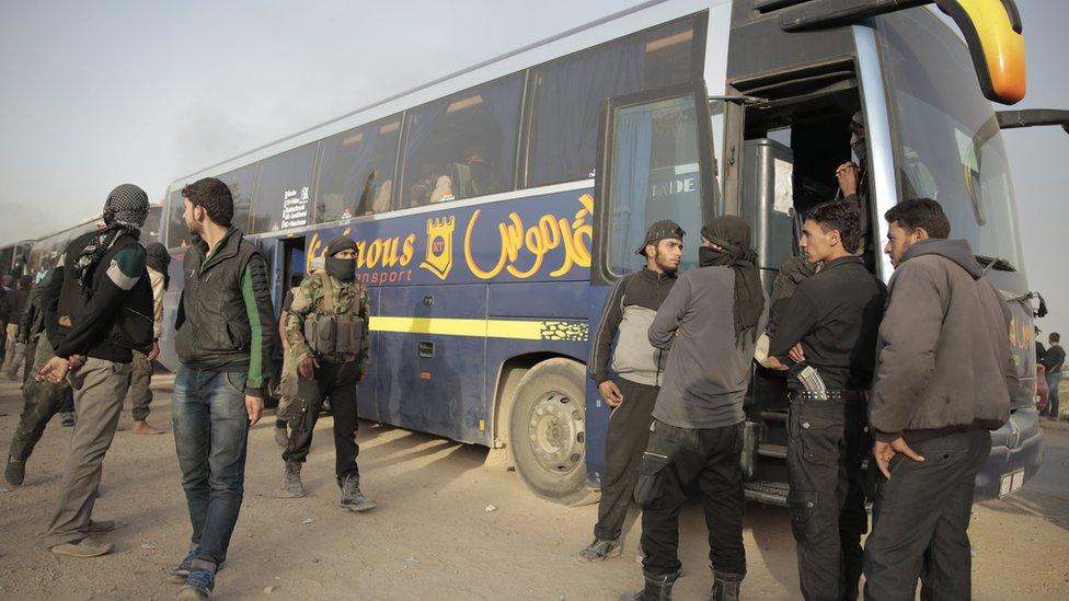 Rebel fighters stand near government-supplied buses in the countryside of Damascus, Syria, on 26 March 2018