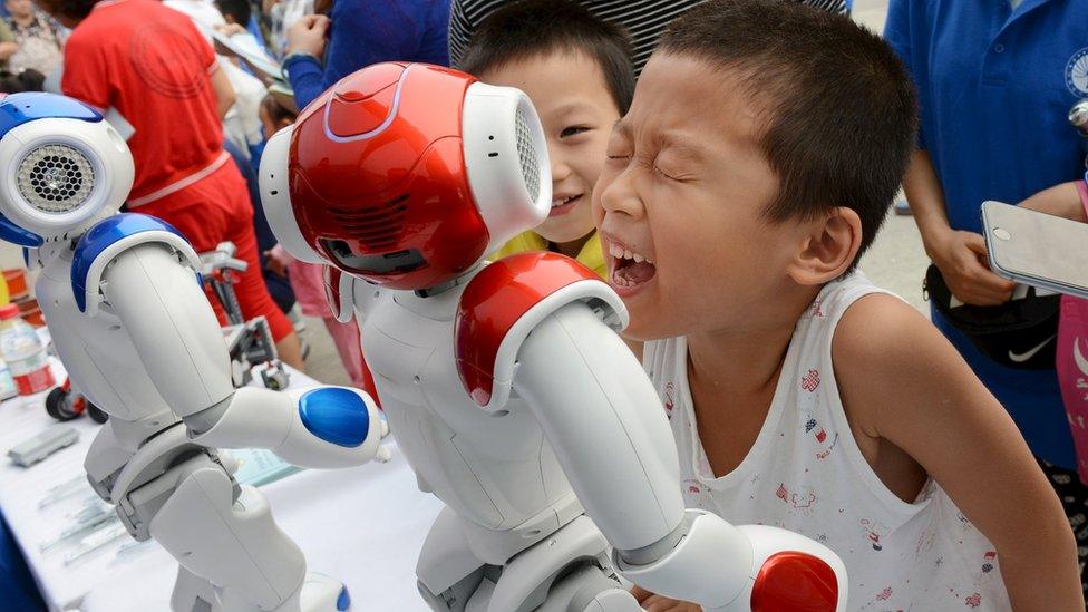 A boy tries to talk to a humanoid robot in Shengzhou, China