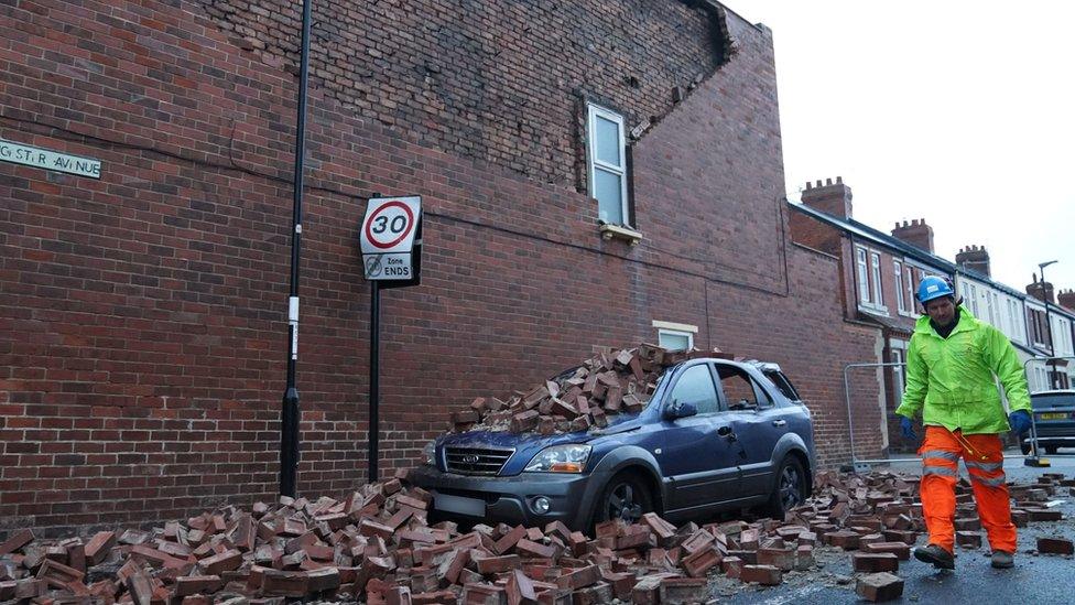 Fallen bricks from the gable end of a property in Sunderland cover the street and a car below