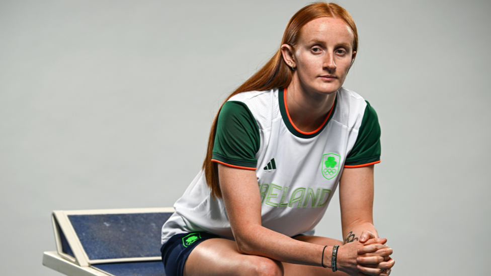 A red headed woman sitting down wearing a green white and orange Team Ireland Olympic kit