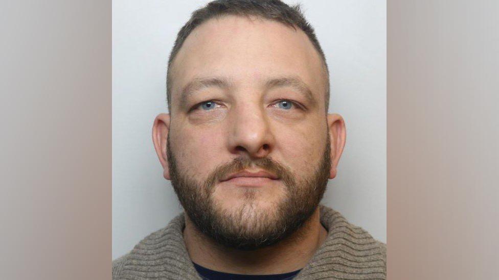 Police custody image of Scott David - he has facial hair and is wearing a grey top