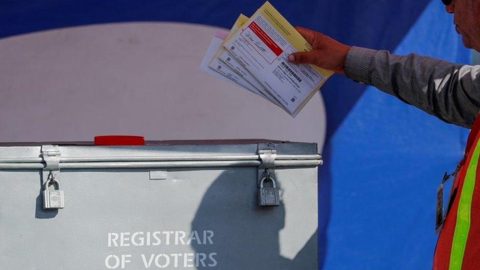 An election worker places mail-in ballots into an election box