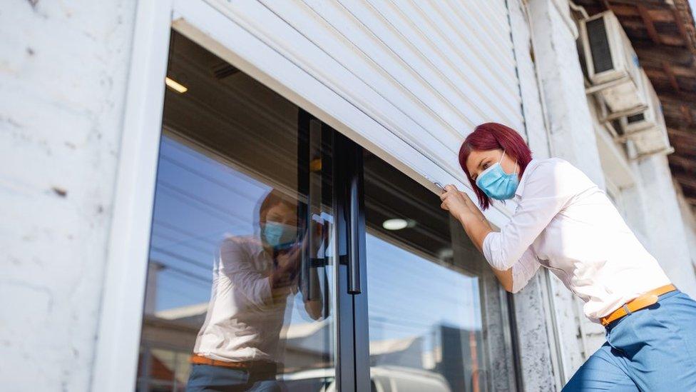 Woman pulls shutters down on a shop