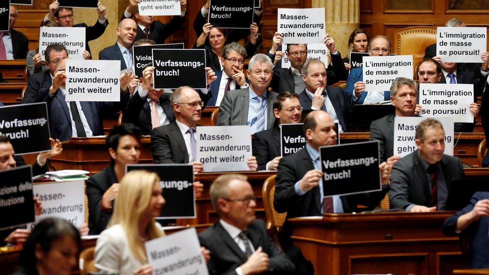 Deputies from the Swiss People's Party hold posters reading "constitutional breach" and "mass immigration continues" after the vote on giving Swiss jobseekers priority in parliament in Bern, Switzerland on 16 December 2016