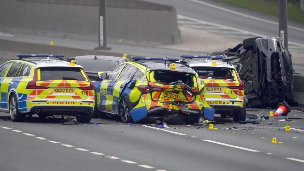 Three police cars and a police van in the middle of the empty A1. One looks damaged from the back. A normal car is on its side next to the central reservation.