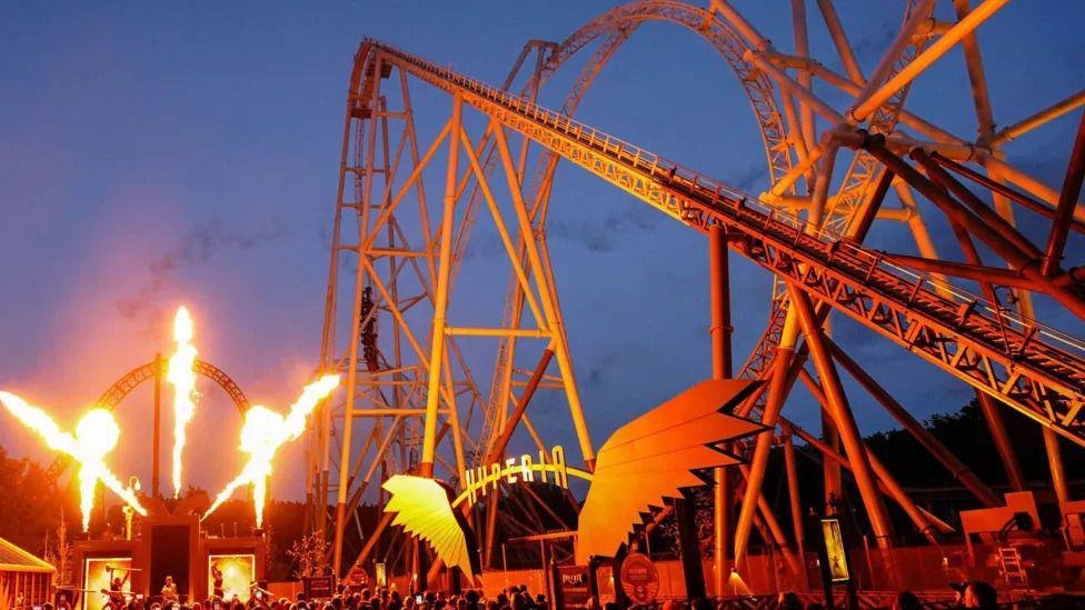 Flames shot from a cannon next to a roller coaster at night