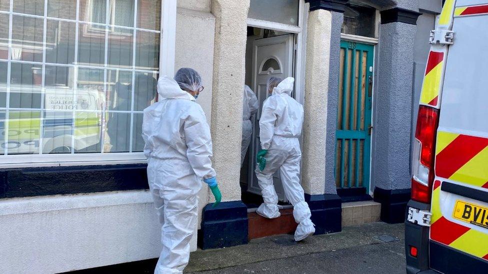 Police in white suits enter the house