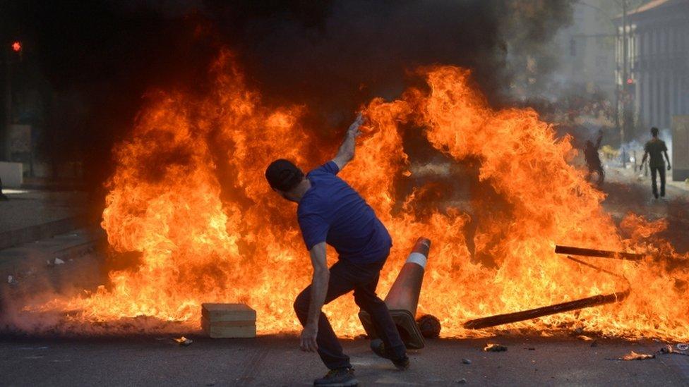 A protester throws a cone in a fire as he protests against spending cuts, 6 December