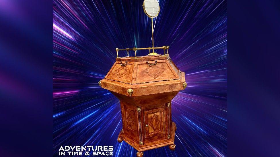 A wooden TARDIS console is in the middle of the image with a purple and blue background.