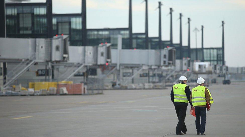 Two workers stand on the tarmac next to the main arrivals and departures hall of the unfinished Willy Brandt Berlin Brandenburg International Airport on 4 Nov, 2014