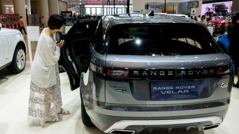 A woman looks at a Range Rover in a car dealership in China