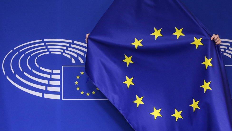 A man adjusts the European flag against a stage illustrated with the hemicycle of the European Parliament