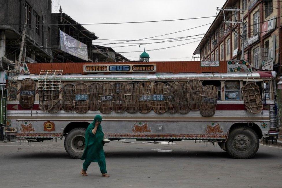 Kashmiri woman walks past a bus used as a road block by Indian security personnel during restrictions after the scrapping of the special constitutional status for Kashmir by the government, in Srinagar