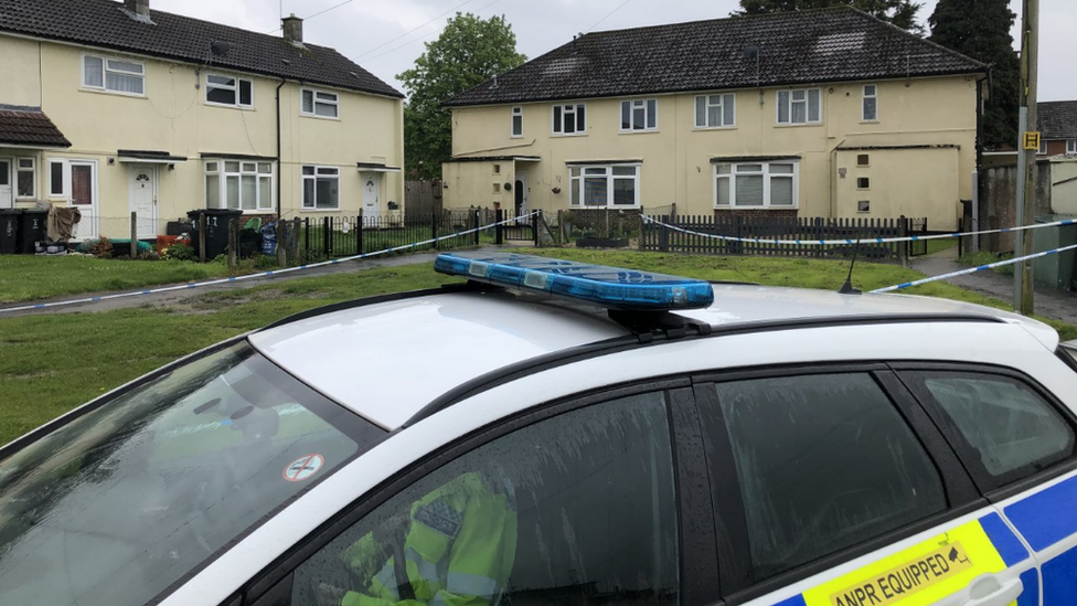 A police car with a grassy area behind it, surrounded by police tape