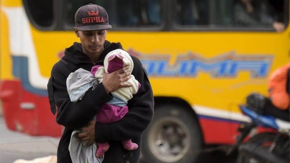 A Venezuelan migrant carries a baby at an improvised camp near a bus terminal in Bogota on September 11, 2018.