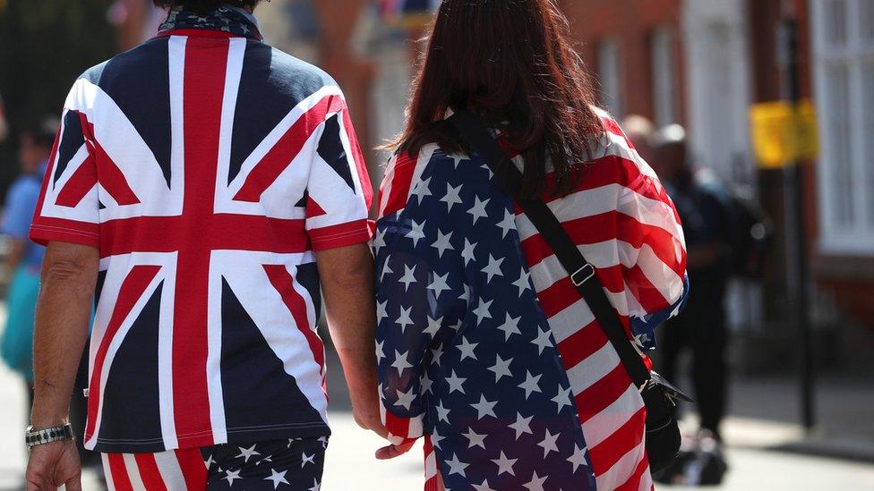 A couple wearing Union Jack and US flags hold hands near Windsor Castle