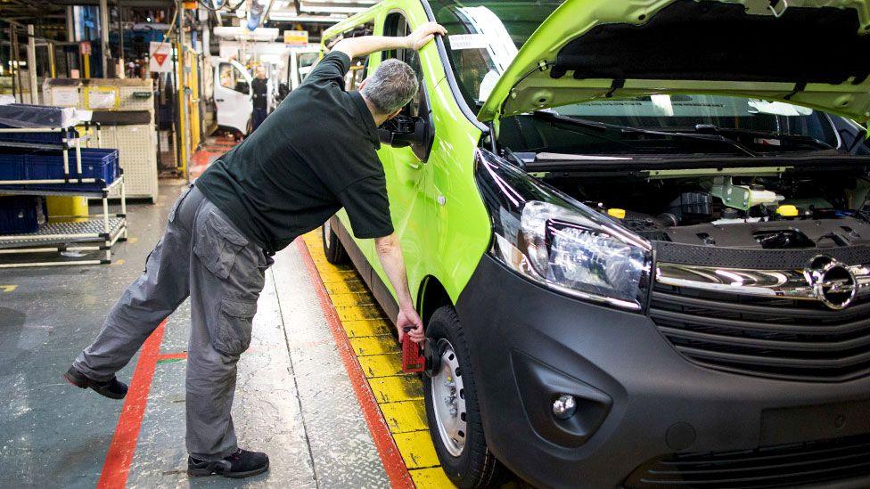 A male employee checks the front wheel of a green Opel Vivaro medium sized van on the final assembly line at the Vauxhall plant in Luton, UK.