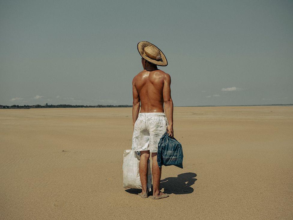 A man wearing just shorts and a sunhat stares out into the distance