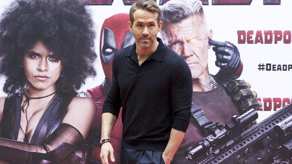 Ryan Reynolds in fron of a Deadpool poster